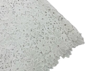 May include: White lace fabric with a delicate floral pattern. The lace has a scalloped edge.