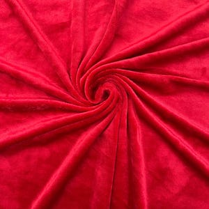 May include: A close-up of a soft, red fabric with a plush texture. The fabric is folded and draped, creating a swirling pattern.