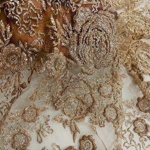 May include: Gold glitter fabric with a floral pattern. The fabric is sheer and has a delicate texture.