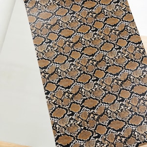 Könnte beinhalten: Brauner und schwarzer Stoff mit Schlangenhautmuster. Das Muster ist ein sich wiederholendes Design aus überlappenden Schuppen.