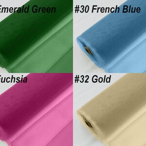 May include: Four rolls of tulle fabric in different colours: emerald green, French blue, fuchsia, and gold. The fabric is rolled up and the ends are visible.