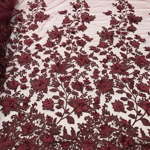 May include: Burgundy floral lace fabric with 3D flowers and beads. The lace has a delicate mesh background and is perfect for adding a touch of elegance to any project.