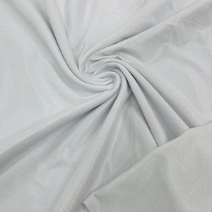 May include: White fabric with a subtle sparkle, showing the texture of the material. The fabric is folded and draped, creating soft folds and curves.