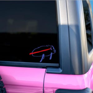May include: A purple and red sticker of a buffalo with a red line through it is affixed to the rear window of a pink vehicle. The vehicle is parked on a beach with palm trees in the background.
