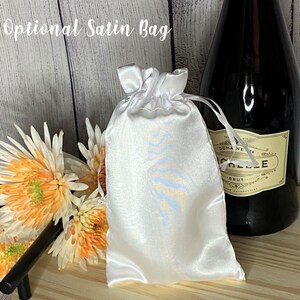 May include: A white satin bag with a blue and white pattern. The bag is tied with a white ribbon and is sitting on a wooden surface.