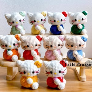 May include: A collection of 10 crocheted Hello Kitty plushies in various colors, including pink, blue, green, yellow, orange, and red. Each plush has a different outfit and a cute expression.