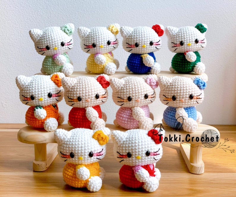 May include: A collection of 10 crocheted Hello Kitty plushies in various colors, including pink, blue, green, yellow, orange, and red. Each plush has a different outfit and a cute expression.