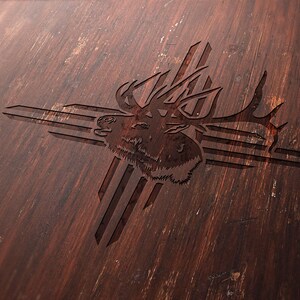May include: A detailed wood carving of an elk head with large antlers, set against a stylized cross design. The carving is set on a dark brown, textured wooden surface, showcasing the natural wood grain.