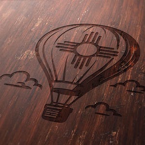May include: A detailed, dark brown wooden surface features an etched hot air balloon design with the New Mexico Zia symbol. The design includes clouds, creating a rustic, vintage aesthetic. The wood grain adds texture.