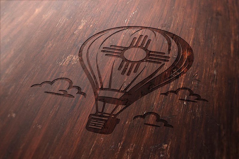 May include: A detailed, dark brown wooden surface features an etched hot air balloon design with the New Mexico Zia symbol. The design includes clouds, creating a rustic, vintage aesthetic. The wood grain adds texture.