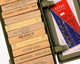 Peut inclure: Une trousse de premiers secours en métal vert olive ouverte, remplie de fournitures médicales. Elle contient des boîtes étiquetées de bandages, de tampons d'iode, d'inhalateurs d'ammoniaque et un kit de brûlures. Épingles de sûreté et instructions.