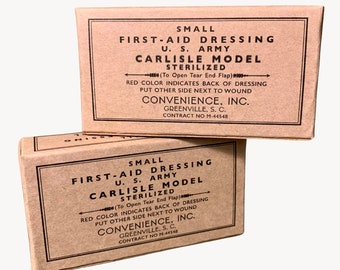 Könnte beinhalten: Zwei braune Pappkartons mit dem Text "SMALL FIRST-AID DRESSING U.S. ARMY CARLISLE MODEL STERILIZED (To Open Tear End Flap) RED COLOR INDICATES BACK OF DRESSING PUT OTHER SIDE NEXT TO WOUND CONVENIENCE, INC. GREENVILLE, S. C. CONTRACT NO M-44548" darauf gedruckt.