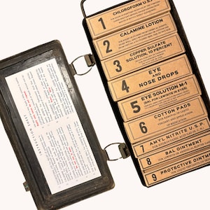 May include: A vintage metal first aid kit with a hinged lid. The kit contains nine labelled compartments, each containing a different type of medical solution. The compartments are numbered 1 through 9. The kit is labelled with instructions for use.
