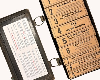 May include: A vintage metal first aid kit with a hinged lid. The kit contains nine labeled compartments, each containing a different type of medical solution. The compartments are numbered 1 through 9. The kit is labeled with instructions for use.