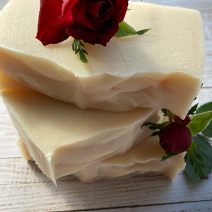 May include: Three bars of white soap stacked on top of each other. The top bar is decorated with a single red rose.