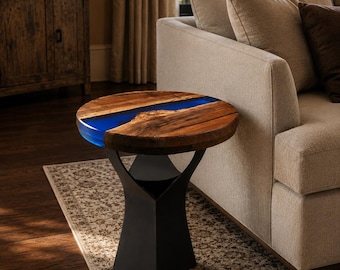 May include: A round side table featuring a natural wood slab top with a prominent blue resin inlay running through the center. The table is supported by a solid black metal pedestal base with a flared design that tapers toward the top.