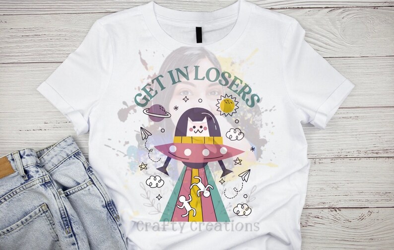 May include: White t-shirt with a colorful graphic of a cat in a spaceship with the text "GET IN LOSERS" printed on it.