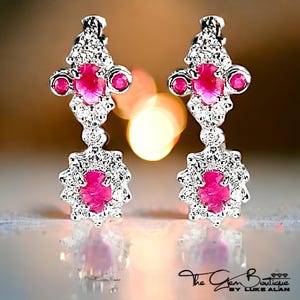 May include: A pair of silver dangle earrings with pink gemstones and a floral design. The earrings have a cluster of small white gemstones surrounding the pink gemstones.