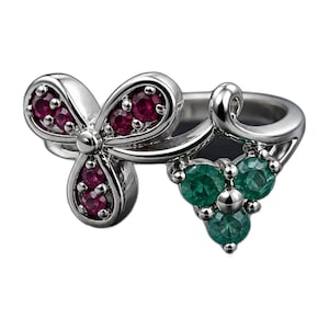 May include: A silver-toned metal ring featuring a floral-inspired design. One side displays a three-petaled shape set with small, round, deep red stones, while the other side features a triangular cluster of three small, round, emerald green stones.