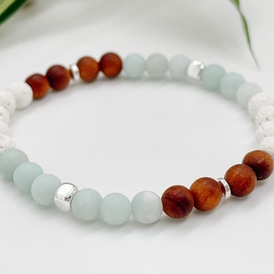 May include: A beaded bracelet with white lava rock, brown wood, and light blue agate beads. The bracelet has silver spacer beads.