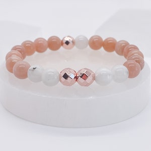May include: A bracelet made with pink and white beads, with two rose gold beads in the centre.