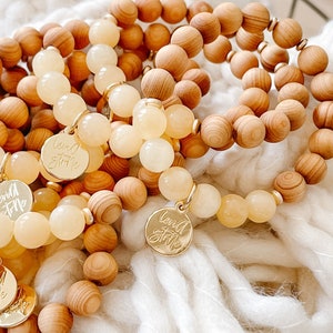 Peut inclure: Gros plan sur plusieurs bracelets en perles de bois et de couleur jaune clair. Les bracelets ont des breloques dorées avec les mots "Love & Style" gravés dessus.