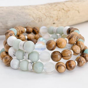 May include: A set of three bracelets featuring wooden beads, white howlite beads, green aventurine beads, and iridescent glass beads.