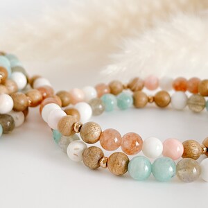 May include: A set of beaded bracelets featuring a combination of light brown wood, pale pink, light green and white beads.
