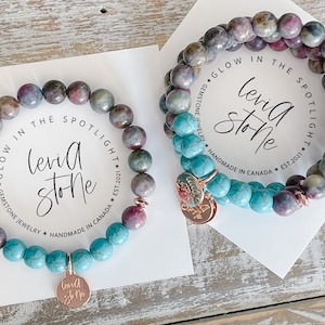 May include: Two bracelets featuring turquoise and pink and green gemstone beads. The bracelets have gold charms with the text "Levid Stone" on them. The bracelets are displayed on a white card with the text "Glow in the Spotlight * Gemstone Jewellery * Handmade in Canada * Est. 2021" on the card.