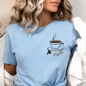 May include: A light blue t-shirt with a graphic of a coffee cup and the word "Coffee" printed on the front.