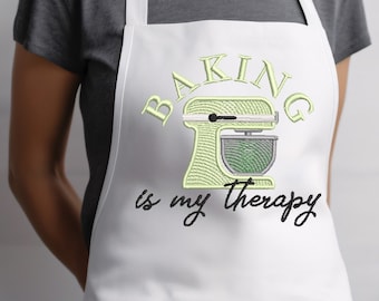 May include: White apron with a pocket and the text "Baking is my therapy" in black script. A green and white illustration of a stand mixer is above the text.