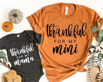 May include: Two matching shirts with a Thanksgiving theme. The larger shirt is orange and says "thankful for my mini". The smaller shirt is gray and says "thankful for my mama".