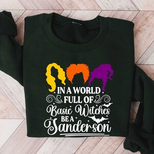 May include: A dark green sweatshirt with a white graphic print that says "In a world full of basic witches be a Sanderson". The graphic also includes three witches with orange, red, and purple hair.