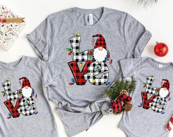 Könnte beinhalten: Ein Set aus drei grauen T-Shirts mit einem rot-schwarz karierten Gnom mit weißem Bart und roter Mütze. Der Gnom hält eine Lichterkette, die "LOVE" buchstabiert.