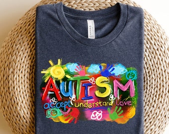 May include: A dark gray t-shirt with a colorful graphic design that says "AUTISM accept understand love". The graphic is made up of hand-drawn shapes and letters.