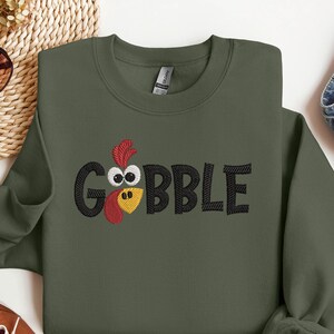 May include: A green sweatshirt with an embroidered turkey design and the word "GOBBLE" in black lettering.