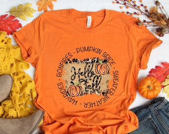 May include: Orange t-shirt with a graphic design that says "Hello Fall" with pumpkins and a burlap background. The graphic is surrounded by text that says "sweater weather - hayrides - bonfires - pumpkin spice".