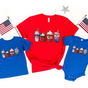 May include: Red, white and blue themed shirts featuring a graphic of five iced coffee drinks. The shirts are in different sizes for adults and children.