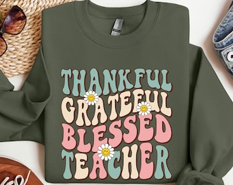 May include: A green sweatshirt with the text "Thankful Grateful Blessed Teacher" in a retro font with daisy accents.