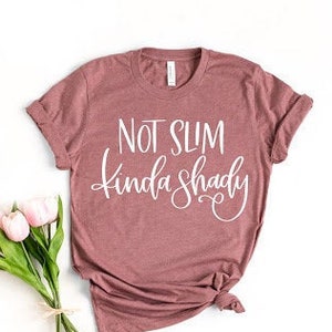 May include: A mauve colored t-shirt with the text "Not Slim Kinda Shady" in white lettering.