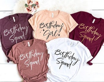 Op de afbeelding: Vijf T-shirts met de tekst "Birthday Squad" in verschillende kleuren. De shirts zijn bordeauxrood, wit, beige en bordeaux.