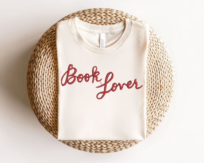 K&ouml;nnte beinhalten: Ein wei&szlig;es T-Shirt mit den Worten "Book Lover" in roter Kursivschrift.
