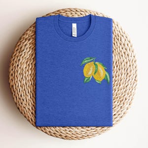 Puede incluir: Una camiseta azul real con un dise&ntilde;o de lim&oacute;n bordado. Los limones son amarillos con hojas verdes.