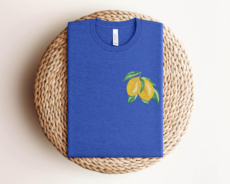 Puede incluir: Una camiseta azul real con un dise&ntilde;o de lim&oacute;n bordado. Los limones son amarillos con hojas verdes.