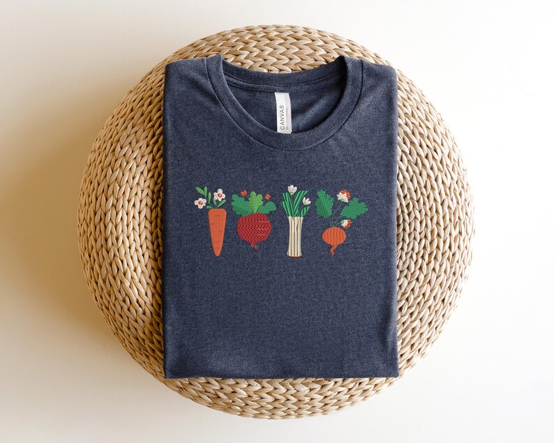 May include: A dark grey t-shirt with an embroidered design of a carrot, beetroot, onion, and radish with green leaves and white flowers.