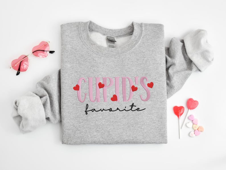 May include: A gray sweatshirt with the text "Cupid's favorite" in pink lettering with red hearts.