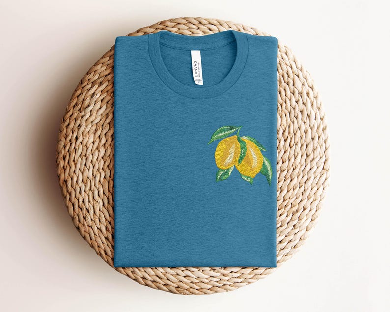 Puede incluir: Una camiseta azul turquesa con un dise&ntilde;o de lim&oacute;n bordado. El lim&oacute;n es amarillo con hojas verdes.