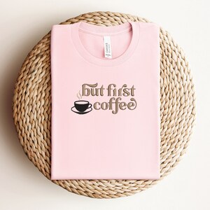 May include: Pink t-shirt with the text "But first, coffee" in brown lettering. A small black coffee cup with steam is above the word "coffee".