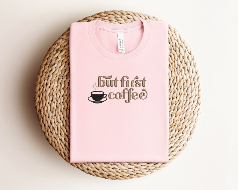 May include: Pink t-shirt with the text "But first, coffee" in brown lettering. A small black coffee cup with steam is above the word "coffee".