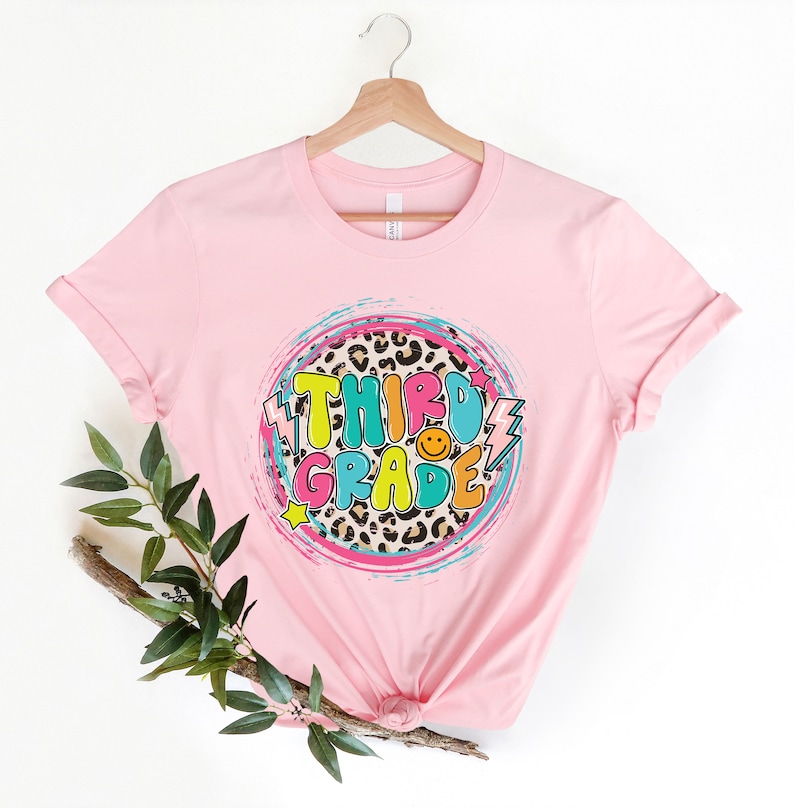 May include: Pink t-shirt with a colorful "Third Grade" graphic on a leopard print background.
